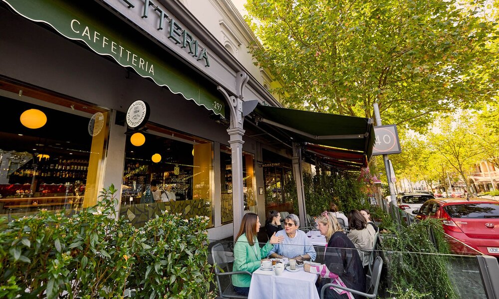 A group of women dining outside a cafe among greenery.