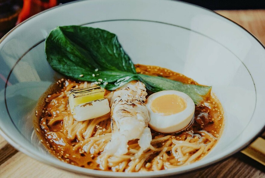 White bowl of ramen with pork, egg and vegetables.