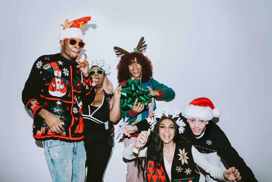 A group of five friends dressed up in Christmas fare posing for a fun photo together.