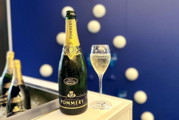 A bottle of Pommery champagne and a full glass beside it against a dark blue background