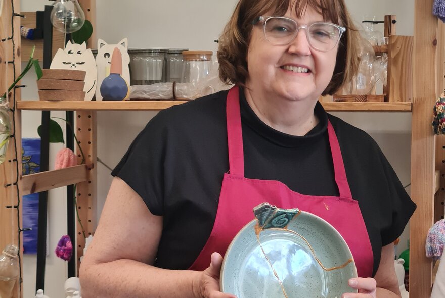Person holding a broken plate mended with gold glue and mismatched patterned inset.