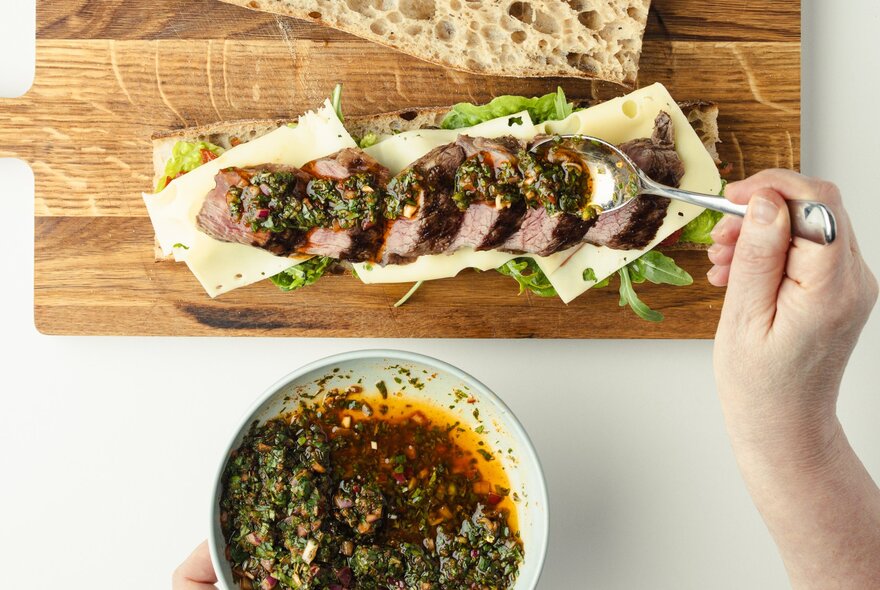 Hand drizzling sauce over a long meat and cheese sandwich.