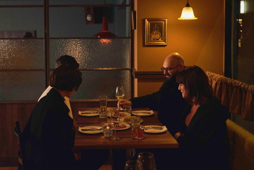 A group of four diners seated at a table inside a dimly lit restaurant.