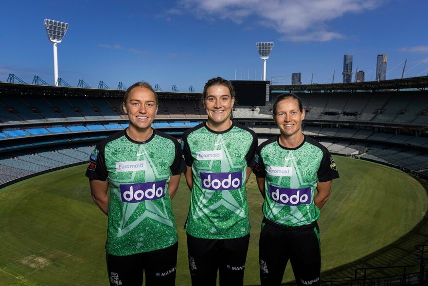 Three players from the Melbourne Stars WBBL team wearing green and black uniforms, posing in front of the MCG.