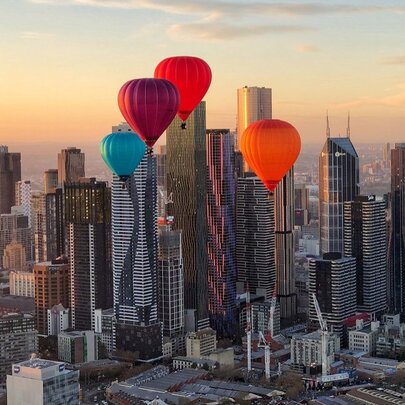 Four hot air balloons floating in front of the Melbourne city skyline during sunrise, with skyscrapers visible in the background.