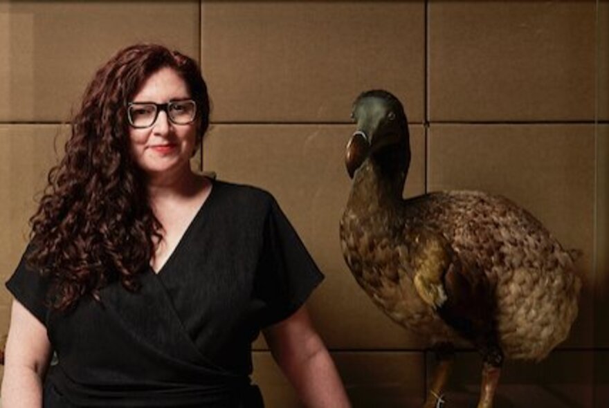 A woman wearing glasses and a black dress, standing next to a museum display of a large bird.