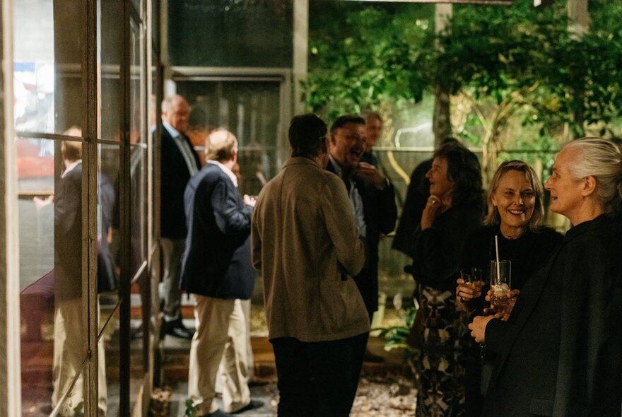 People standing with cocktails in a garden and house setting.