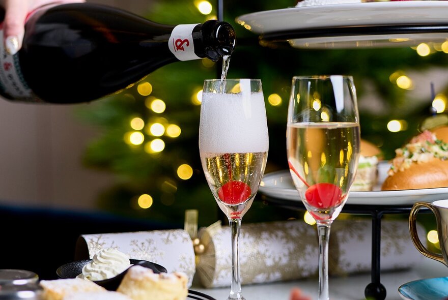 Sparkling wine being poured into two flute glasses as part of a high tea spread.