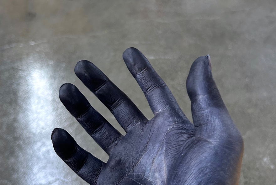 A hand dyed with blue textile ink, against a shiny concrete floor.
