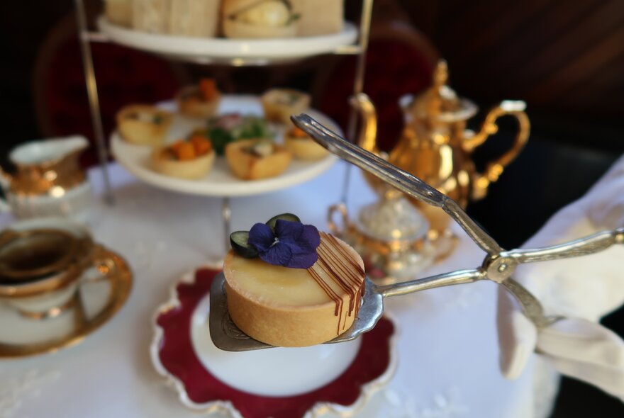 Silver service tongs placing a tart on a plate.