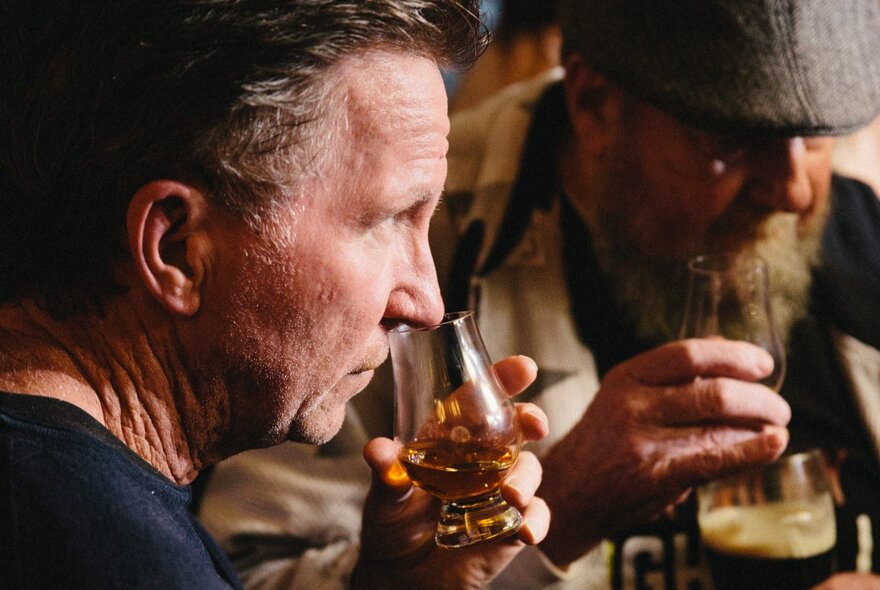 Two men smelling and tasting whisky in a bar setting.