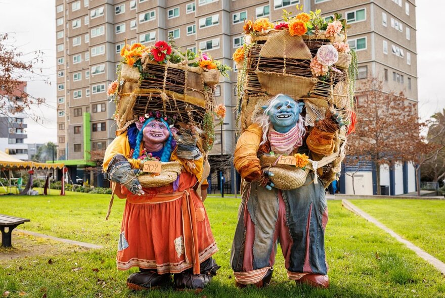 Interactive roving puppet performers of oversized mythical creatures bearing baskets of flowers and produce, on the lawns in front of the Carlton Highrise Estate.
