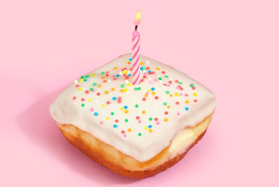 A square-shaped doughnut with white icing, colourful sprinkles and a candle.