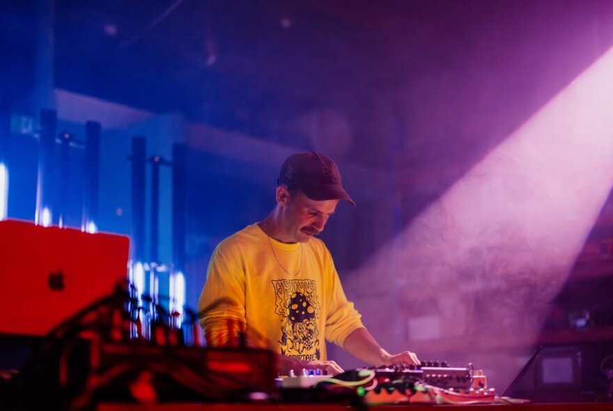 usician performing at a keyboard and sound desk under smoky purple light.