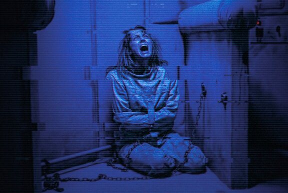 An asylum inmate huddled in the corner of a padded room screaming and wearing a straight jacket.