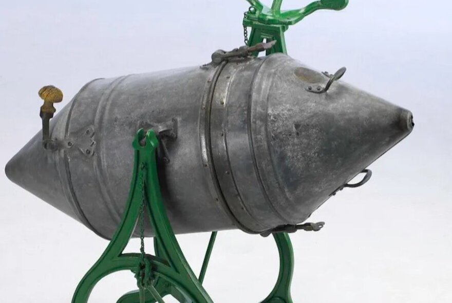 Old form of washing machine, metal contraption with lids on green metal stand.