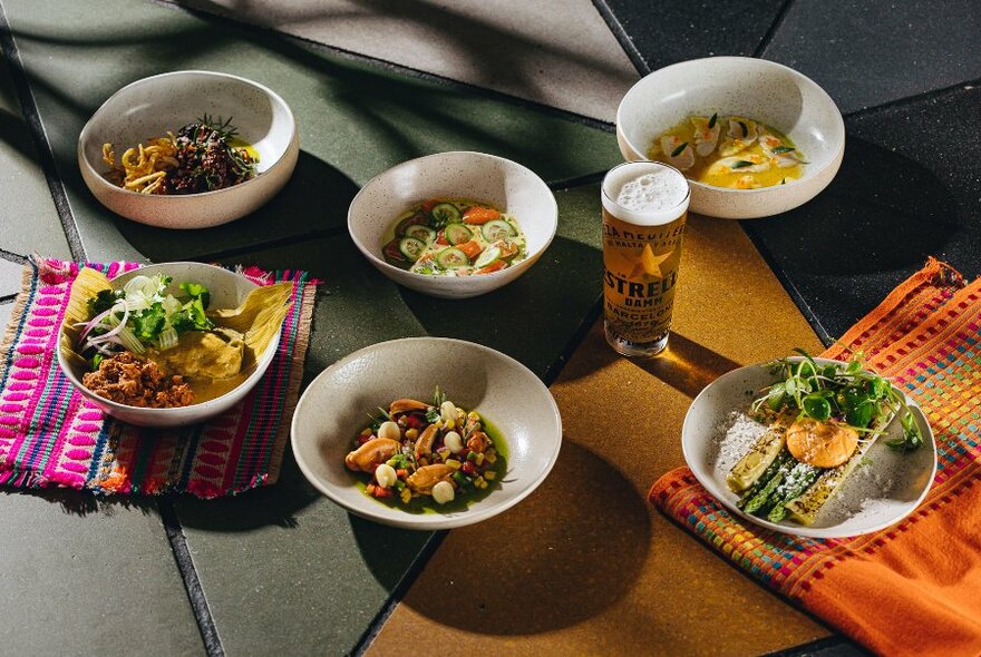 A table with several dishes including salads, snacks, meats and a glass of beer.