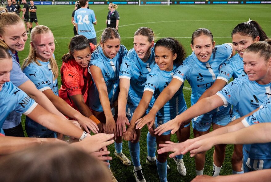 A women's soccer team put their hands in together on a football field. 