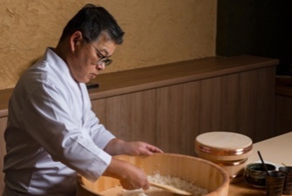 Japanese chef mixing rice in a large wooden barrel.