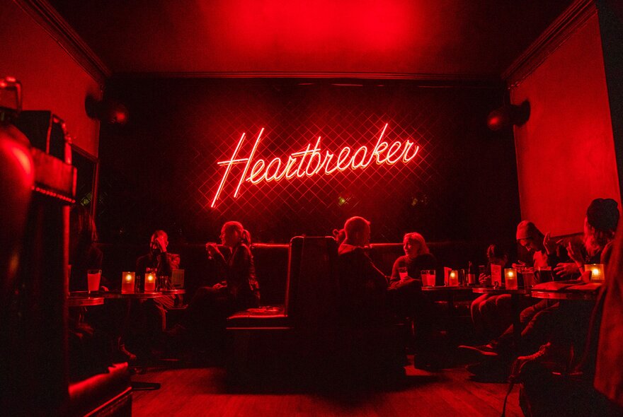 The dark, red interior of a club with a neon Heartbreaker sign on the back wall. 