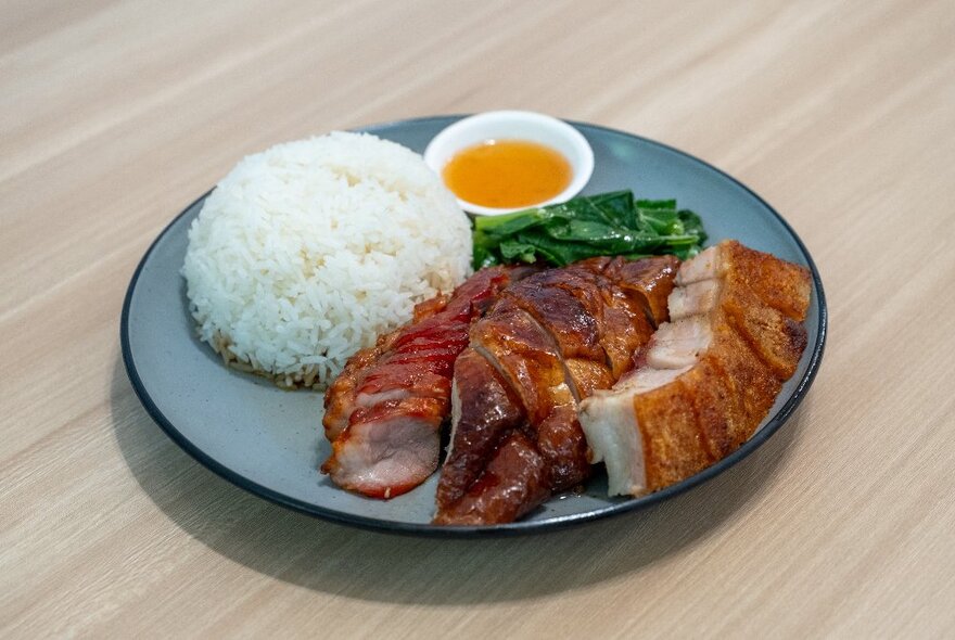 A plate of Kong Kong-style food, with white rice, sliced barbecued meats and Chinese broccoli.