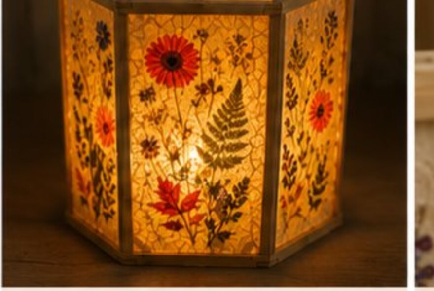 A decorated lampshade featuring homemade paper and pressed flowers wth a warm yellow glow from the LED globe inside. 