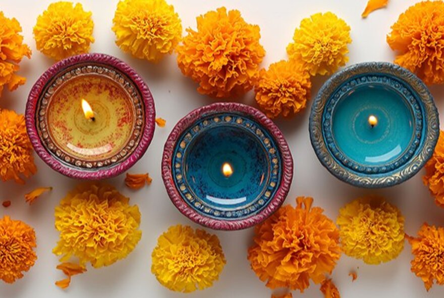 Looking down at three Diwali clay lamps, surrounded by yellow and orange flowers.