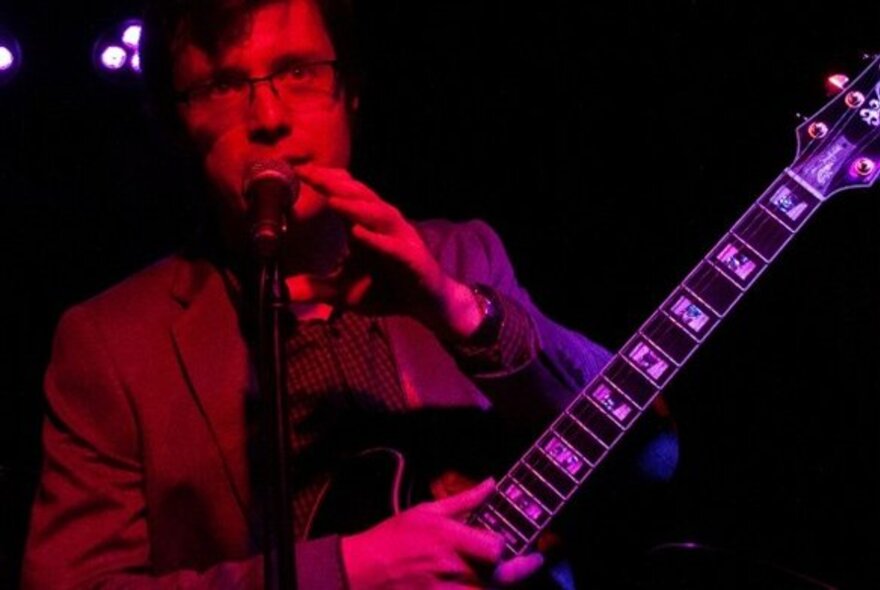 Guitarist performing on stage under red lights.