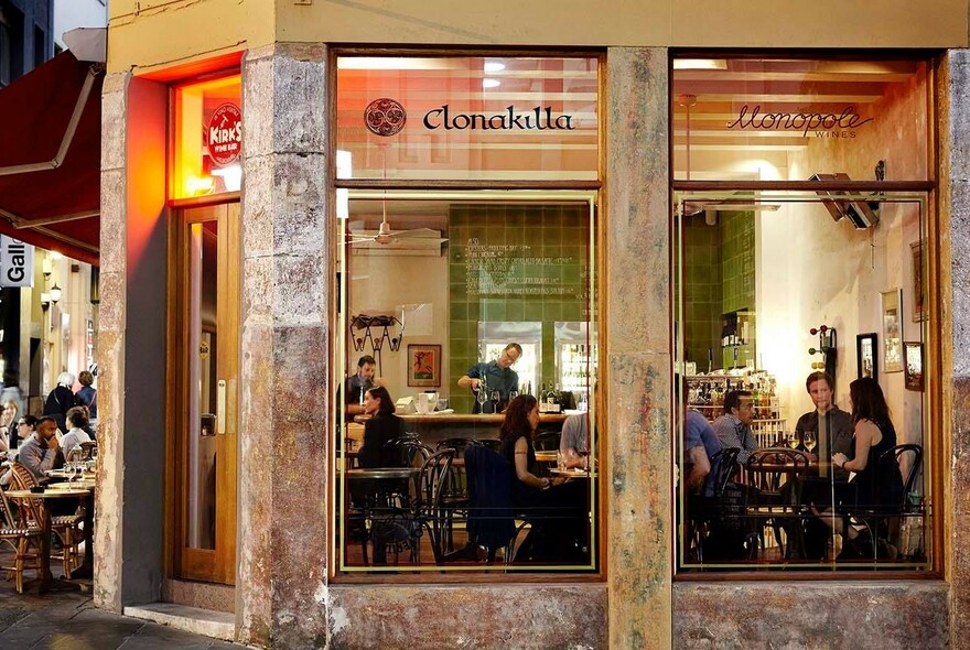 View of Kirk's Wine Bar from the street with people seated at small tables, seen through large windows.