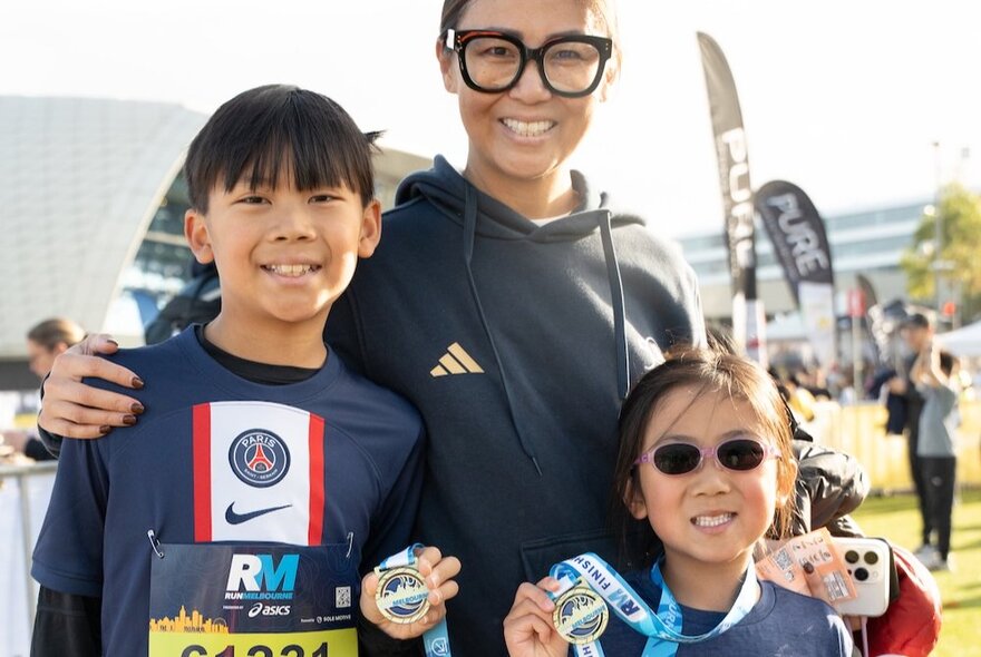A mother and her two children who are both holding up finishing medals for the kids dash at the Run Melbourne event.
