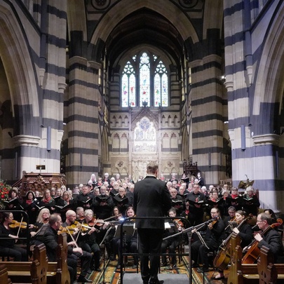 A conductor and orchestra inside a grand cathedral space.