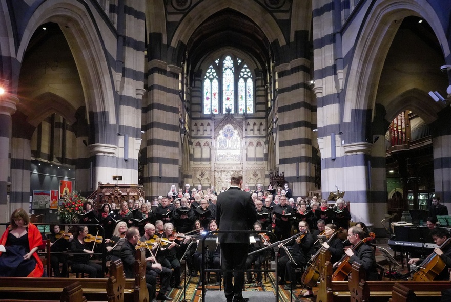 A conductor and orchestra inside a grand cathedral space.