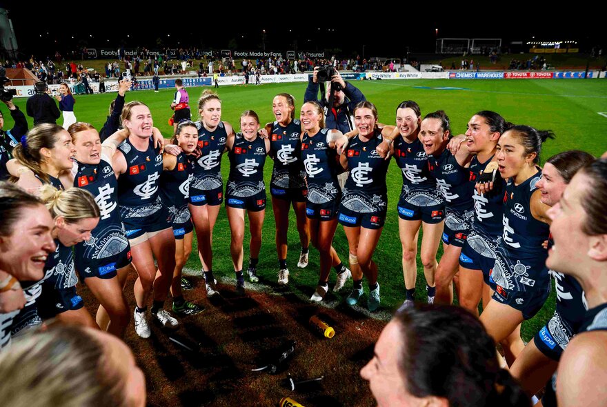 Carlton AFLW players in a circule during a match.