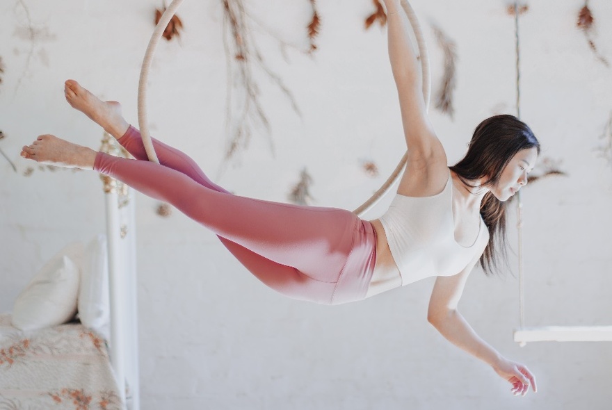 Person balanced in an aerial hoop, legs extended behind her, against a white wall.
