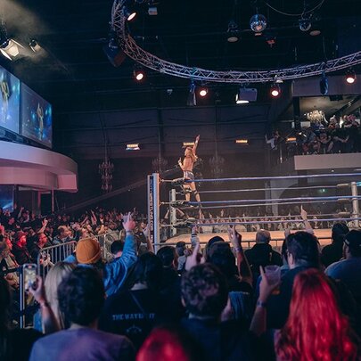 A large crowd watching a wrestling match with two fighters in a ring. 