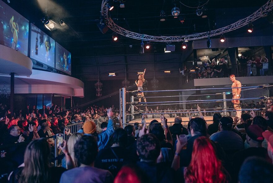 A large crowd watching a wrestling match with two fighters in a ring. 