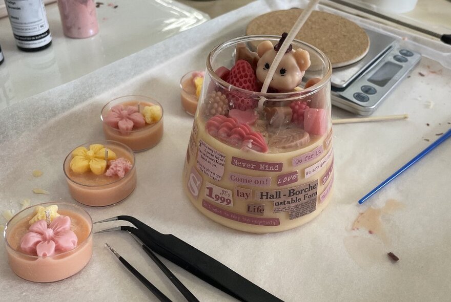 Flower-topped candles in small dishes next to a larger candle with toys, with equipment nearby.