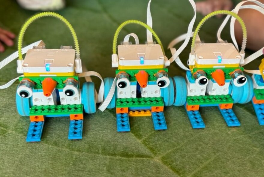 Three robotic LEGO models of birds with googly eyes, resting on a green leaf-like carpet.