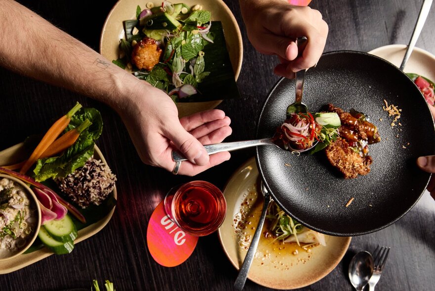 Chef's hands moving food from a pan into dishes.