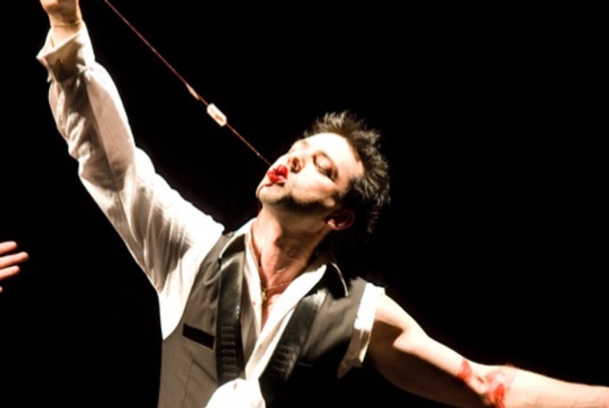 A magician pulling something long and straight out of his mouth in a performance.