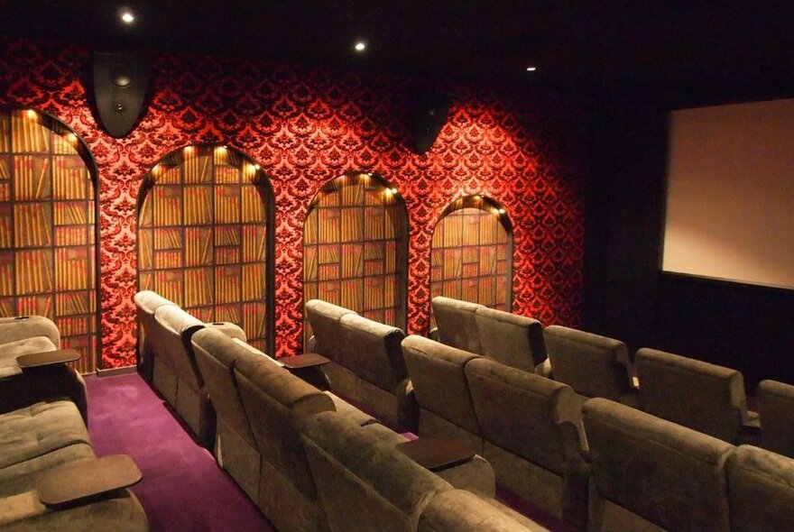 Rows of comfortable chairs in a cinema, with decorated walls, soft down lights and the edge of a cinema screen visible.