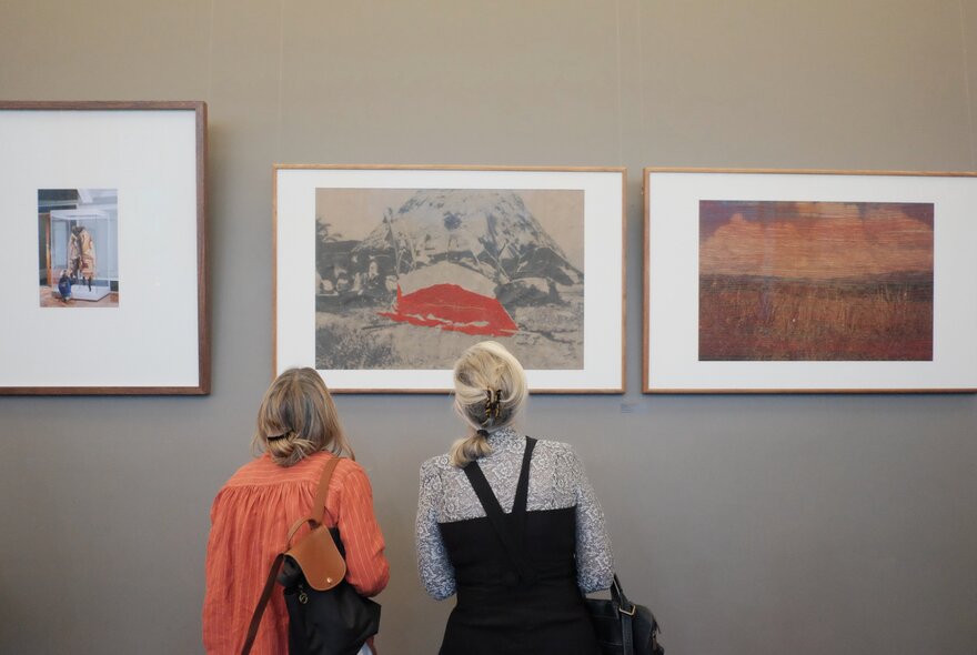 The back of two woman looking at framed art on the wall of a gallery