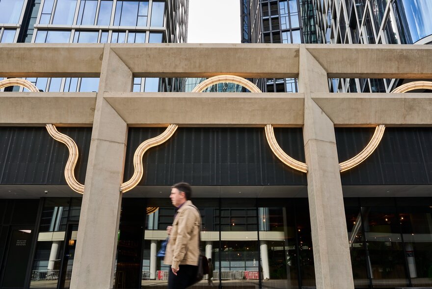 A structural artwork in front of a city building, with a pedestrian walking past.