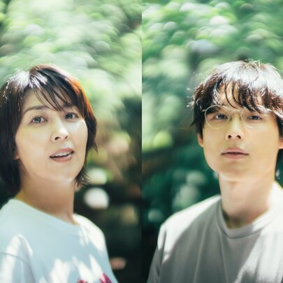 Japanese actors Takako Matsu and Hokuto Matsumura standing side by side outdoors against a green leafy backdrop, in a still from the romantic drama film 1st Kiss.