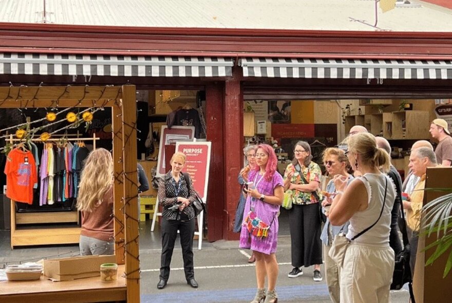 A group of people who have stopped to listen to a speaker on a tour at the Queen Victoria Market, Melbourne. 