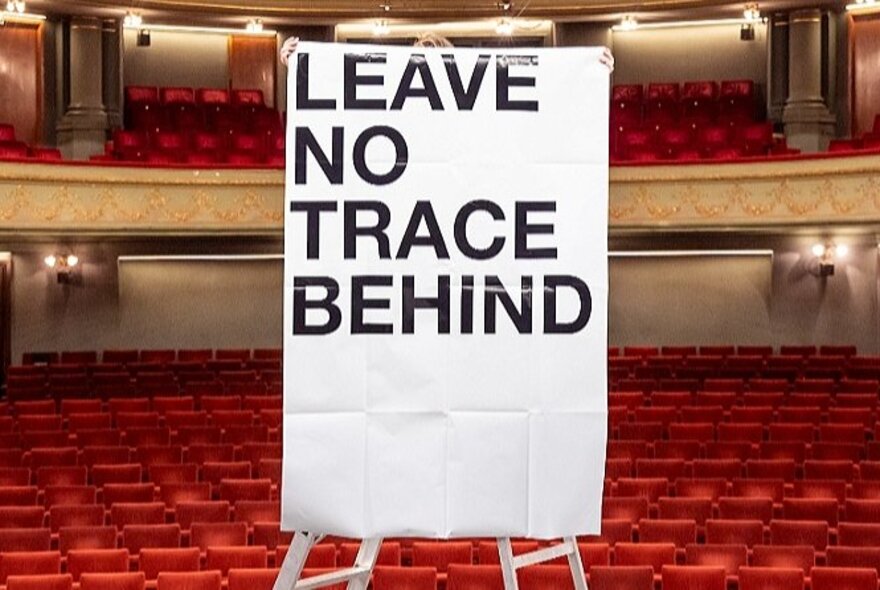 A large sign on a bard in a carpeted theatre auditorium.