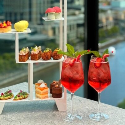 Display of cakes with two glasses of red drink, Yarra River in background.