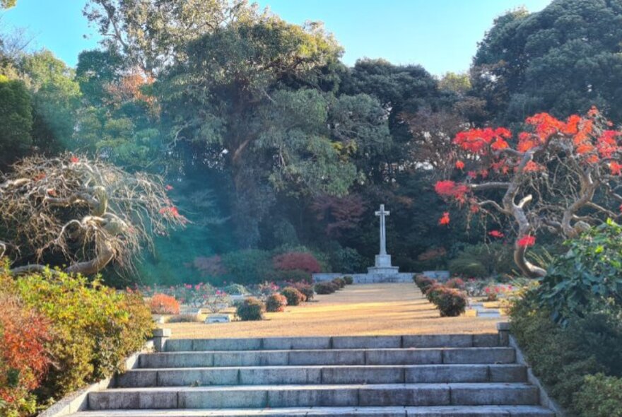 Steps in a landscaped garden leading to a memorial cross, at the Yokohama Commonwealth War Cemetery in Japan.