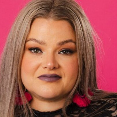 Singer with long grey hair and purple lipstick, hot pink background.