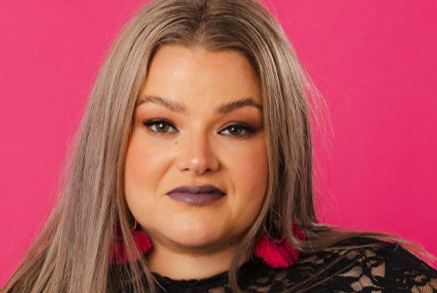Singer with long grey hair and purple lipstick, hot pink background.